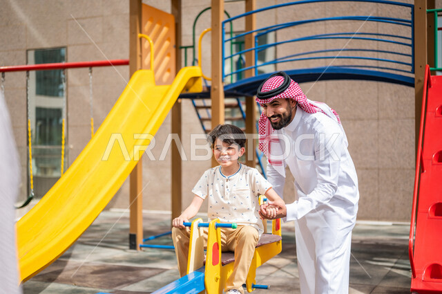 رجل عربي خليجي سعودي يقضي وقت ممتع مع ابنه  ، الاستمتاع باللعب بالالعاب الترفيهية  ، التسلية والترفيه ،مشاركة الاطفال بالانشطة الترفيهية ، انشطة صيفية ترفيهية ، قضاء وقت عائلي ممتع، عطلة صيفية سعيدة 