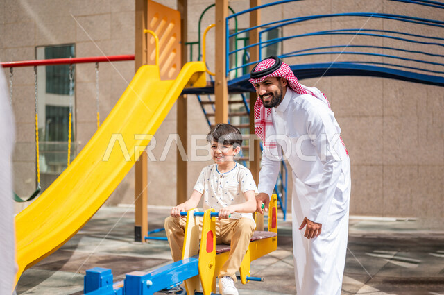 رجل عربي خليجي سعودي يقضي وقت ممتع مع ابنه  ، الاستمتاع باللعب بالالعاب الترفيهية  ، التسلية والترفيه ،مشاركة الاطفال بالانشطة الترفيهية ، انشطة صيفية ترفيهية ، قضاء وقت عائلي ممتع، عطلة صيفية سعيدة 