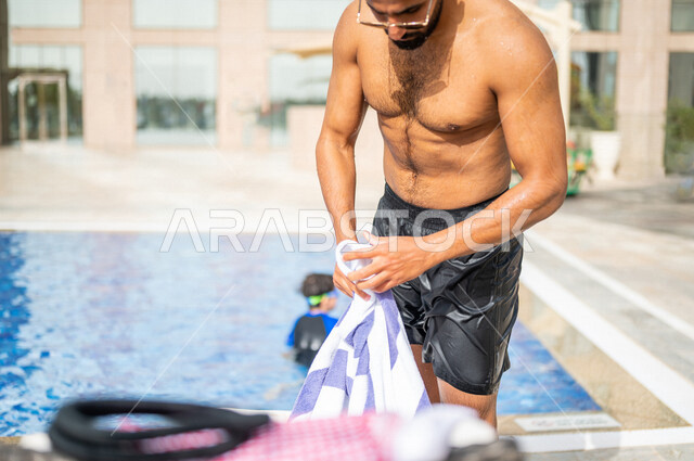 A Saudi Arabian Gulf man using the towel after finishing swimming, swimming pool, chalets and resorts, water entertainment activities, happy summer vacation
