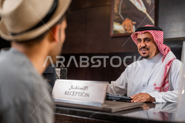 موظف استقبال عربي خليجي سعودي يقوم باستقبال سائح عربي بسعادة ، إجراءات الحجز و الدخول لدى مكتب الاستقبال في الفندق ، خدمة العملاء في الفندق السياحي ، اجراءات الحجز و الاستفسار ، سياحة و فندقة