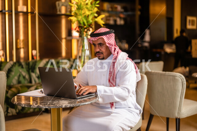 رجل أعمال عربي خليجي سعودي يستخدم الحاسوب المحمول يجلس في أحد الفنادق الخليجية ، انجاز مهام العمل ، تحقيق أهداف الشركة و العمل ، متابعة وتطوير الأعمال ، العمل عن بعد ، كتابة ملاحظات و تقييم الأعمال و المشاريع
