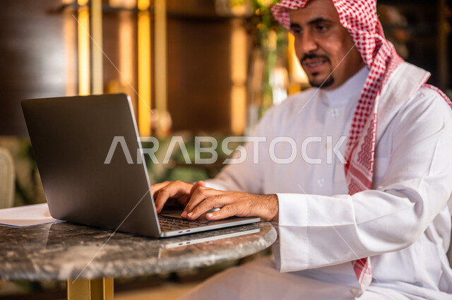 رجل أعمال عربي خليجي سعودي يستخدم الحاسوب المحمول يجلس في أحد الفنادق الخليجية ، انجاز مهام العمل ، تحقيق أهداف الشركة و العمل ، متابعة وتطوير الأعمال ، العمل عن بعد ، كتابة ملاحظات و تقييم الأعمال و المشاريع