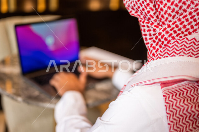 صورة مقربة لرجل أعمال عربي خليجي سعودي يستخدم الحاسوب المحمول يجلس في أحد الفنادق الخليجية ، انجاز مهام العمل ، تحقيق أهداف الشركة و العمل ، متابعة وتطوير الأعمال ، العمل عن بعد ، كتابة ملاحظات و تقييم الأعمال و المشاريع