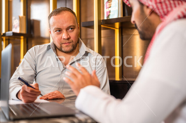 A close-up of two Saudi Arabian Gulf businessmen using a laptop and discussing work, business partners meeting in a Gulf hotel, business agreement, partnership on business and commercial projects, business deals and cooperation between companies