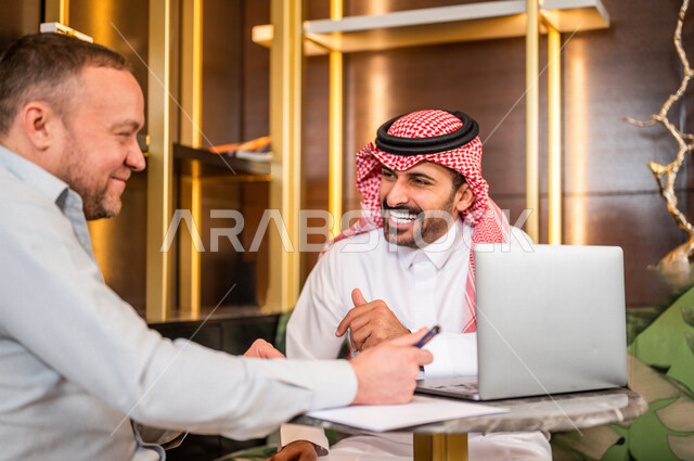 رجل أعمال عربي خليجي سعودي يقوم بتوقيع عقد عمل بسعادة ، شركاء عمل يجتمعان في أحد الفنادق الخليجية ، إتفاق عمل جديد ، الشراكة على الأعمال و المشاريع التجارية ، صفقات عمل و تعاون بين الشركات