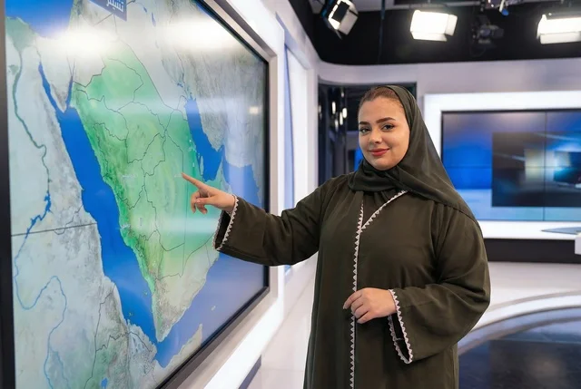 Saudi Female News Presenter Pointing at Screen in Studio