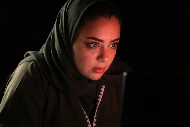 امرأة سعودية محجبة تنظر بذهول وصدمة إلى شاشة مضيئة في الظلام امرأة سعودية محجبة تنظر بذهول وصدمة إلى شاشة مضيئة في الظلام