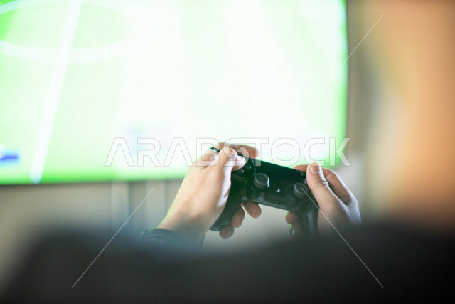 شاب عربي سعودي خليجي يمسك بيده عصا التحكم و يلعب بألعاب الفيديو، المتعة و التسلية بألعاب الفيديو، ألعاب البلايستيشن الترفيهية، تقنيات و ألعاب, قضاء وقت ممتع في المنزل