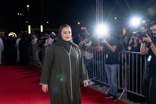 امرأة سعودية بالعباءة الخضراء على السجادة الحمراء