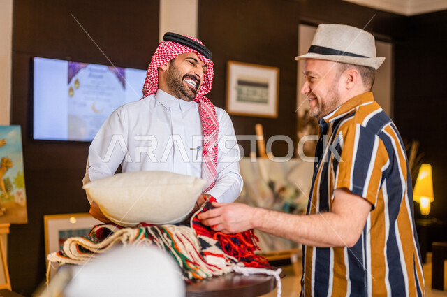 A Saudi Arabian Gulf man working as a tourism guide accompanied by an Arab tourist in casual clothes smiling in one of the Saudi heritage places, watching the Arab Majlis cushions and Al-Sadu embroideries, handicrafts, Saudi heritage, artistic and popular