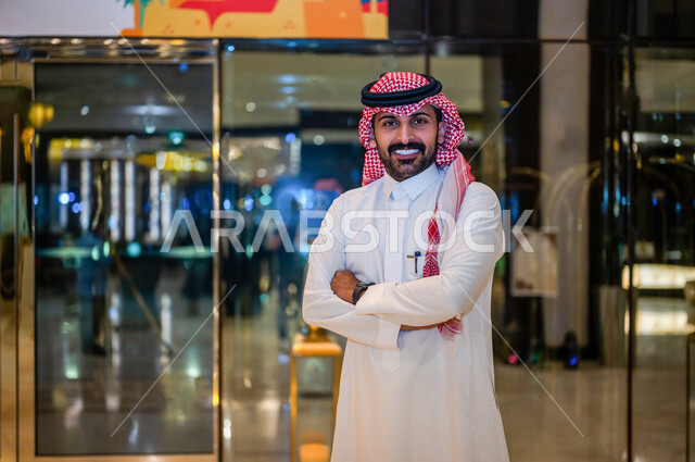 A Saudi Arabian Gulf man standing smiling with clasped hands in one of the Saudi tourist heritage exhibitions, a businessman standing with confidence, Saudi heritage, artistic and popular heritage exhibitions