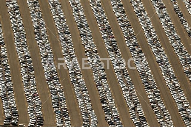 A vast parking lot filled with rows of parked cars, organized in long parallel lines.