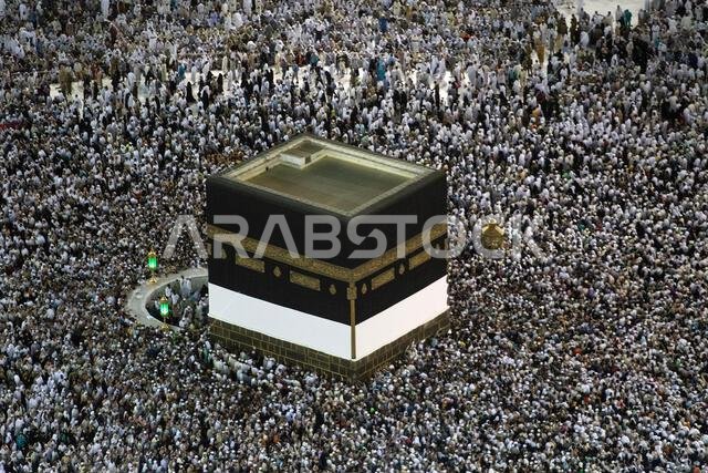 A large crowd of people surrounds the Kaaba in the Masjid al-Haram.