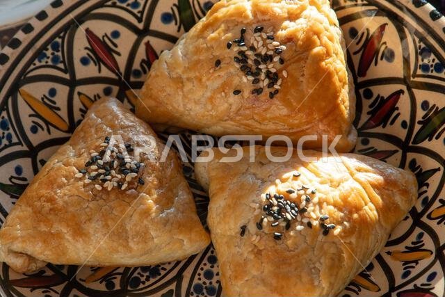 Samosa made from puff pastry dough. A triangular pie with meat filling, sprinkled with sesame seeds. Plate top view
