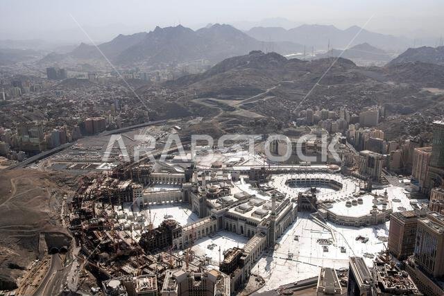 منظر جوي للمسجد الحرام في مكة المكرمة، محاطاً بالمباني الحضرية والجبال.