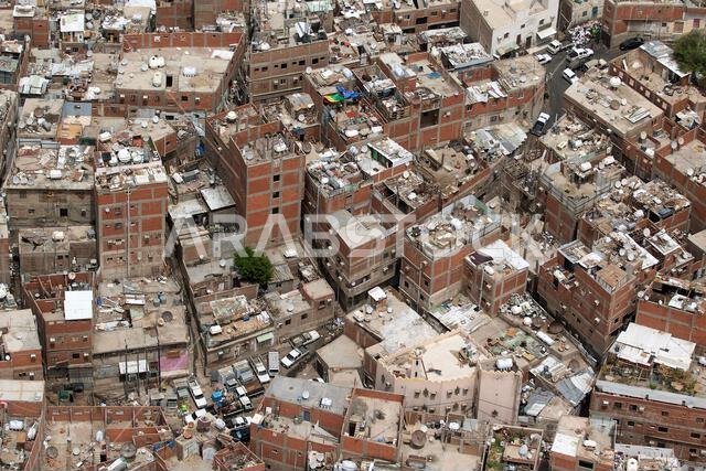 منظر جوي لمبانٍ حضرية مكتظة بالسكان مع العديد من الهياكل على أسطحها ومركبات متناثرة.