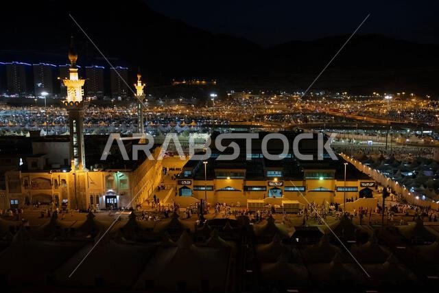 يظهر مجمع مسجد كبير مضاء ليلاً، محاطاً بالعديد من الخيام وحشود من الناس.