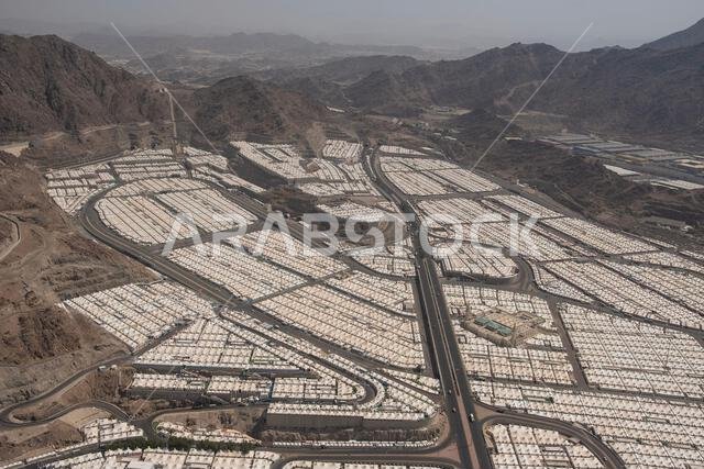 تتميز المناظر الطبيعية الصحراوية الشاسعة بخيام بيضاء عديدة مرتبة في صفوف أنيقة، متصلة بطرق متعرجة ومحاطة بجبال قاحلة. تتميز المناظر الطبيعية الصحراوية الشاسعة بخيام بيضاء عديدة مرتبة في صفوف أنيقة، متصلة بطرق متعرجة ومحاطة بجبال قاحلة.