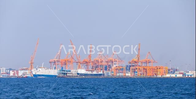 Jeddah, Saudi Arabia - December 22, 2019: Busy container port with rows of orange gantry cranes, cargo ship at dock and stacked containers conveying m