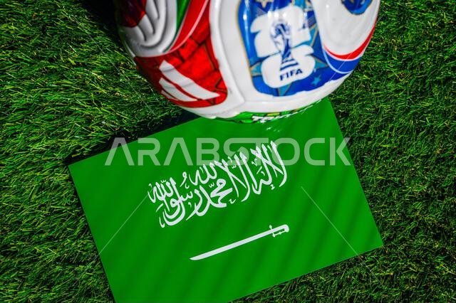علم المملكة العربية السعودية مع كرة مباراة كأس العالم 2026 الرسمية على العشب. خلفية كأس العالم. علم المملكة العربية السعودية مع كرة مباراة كأس العالم 2026 الرسمية على العشب. خلفية كأس العالم.