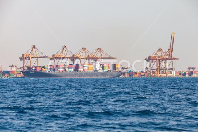 Jeddah, Saudi Arabia - December 22, 2019: Large container ship Ensenada at a busy port terminal with towering gantry cranes and stacked colorful conta