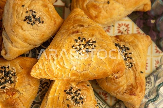 سامسا مصنوعة من عجينة الباف باستري. فطيرة مثلثة الشكل محشوة باللحم، ومزينة ببذور السمسم. صورة من أعلى الطبق