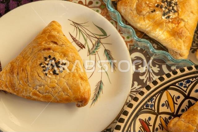سمبوسة مصنوعة من عجينة الباف باستري. فطيرة مثلثة الشكل محشوة باللحم، ومزينة ببذور السمسم. منظر علوي للمأكولات الآسيوية سمبوسة مصنوعة من عجينة الباف باستري. فطيرة مثلثة الشكل محشوة باللحم، ومزينة ببذور السمسم. منظر علوي للمأكولات الآسيوية