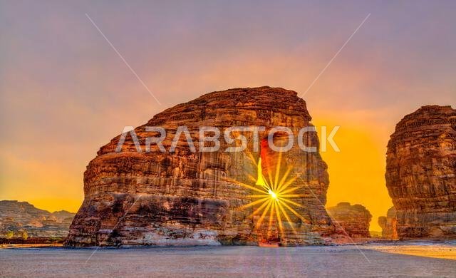 A sunburst shines through the natural arch of Elephant Rock at sunset in AlUla, Saudi Arabia.