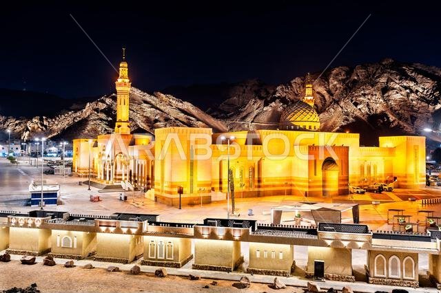 The illuminated Sayyid Al Shuhada Mosque stands at the base of Mount Uhud in Madinah, Saudi Arabia, showcasing Islamic architecture under a night sky.