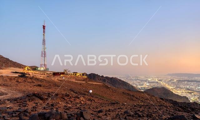 منظر بانورامي خلاب لأضواء مدينة المدينة المنورة من قمة جبل أحد الصخرية عند الغسق مع برج اتصالات في المقدمة.