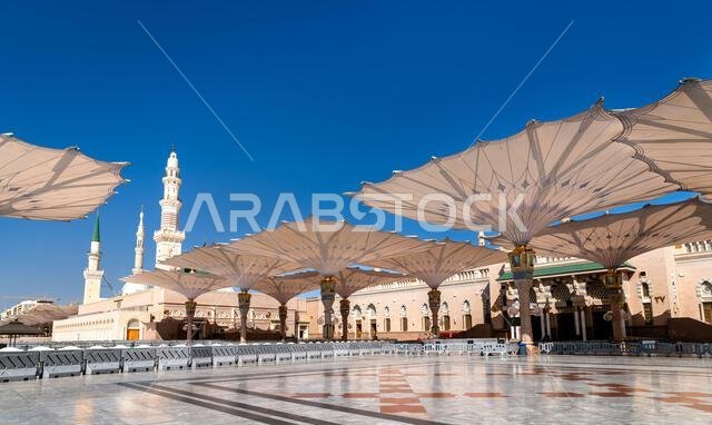 تتميز ساحة المسجد النبوي بمظلات ميكانيكية كبيرة ومآذن تحت سماء زرقاء صافية في المدينة المنورة، المملكة العربية السعودية.