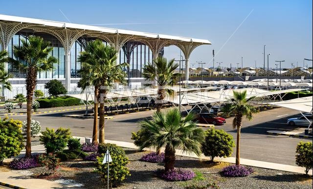 التصميم الخارجي الحديث وتنسيق الحدائق لمطار الأمير محمد بن عبد العزيز الدولي في المدينة المنورة بالمملكة العربية السعودية، ويظهر مبنى الركاب ومنطقة وقوف السيارات.