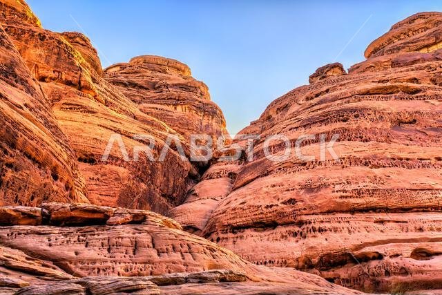 منحدرات رملية حمراء مثيرة وتكوينات صخرية فريدة في جبل إثلب في موقع الحِجر النبطي القديم، العلا، المملكة العربية السعودية.