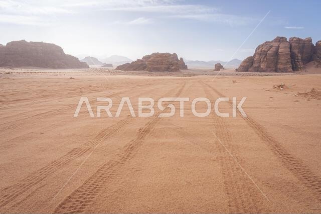 Tire tracks leading through sandy desert landscape with sandstone mountains, Tabuk, Saudi Arabia