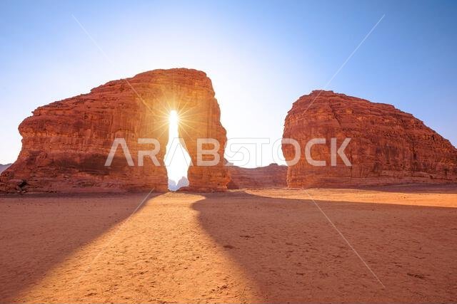 Elephant Rock (Jabal AlFil) towers in AlUla's sandstone desert as the setting sun creates a starburst through its natural arch, casting long golden