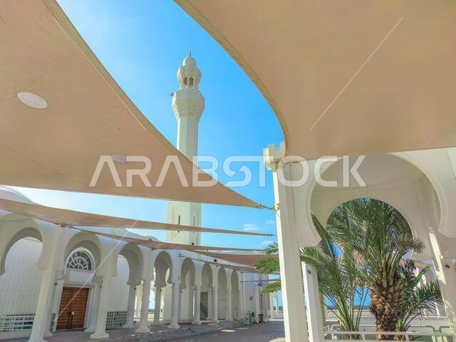 تفاصيل معمارية لمسجد حديث في جدة، المملكة العربية السعودية، تُظهر أقواسًا بيضاء ومئذنة شاهقة في تناغم مع سماء زرقاء صافية.