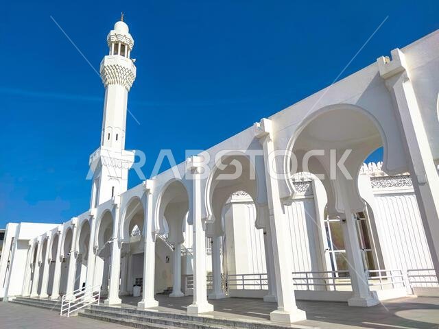 تفاصيل معمارية لمسجد حديث في جدة، المملكة العربية السعودية، تُظهر أقواسًا بيضاء ومئذنة شاهقة في تناغم مع سماء زرقاء صافية.