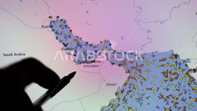Map of Vessel Finder, flows of boats, containers, cargo ships, and freighters in the Strait of Hormuz. Silhouette of a hand with a pen pointing at a