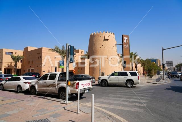 Traditional mud brick watchtower and official entrance sign at Al Dho historical district with street traffic, Riyadh, Saudi Arabia