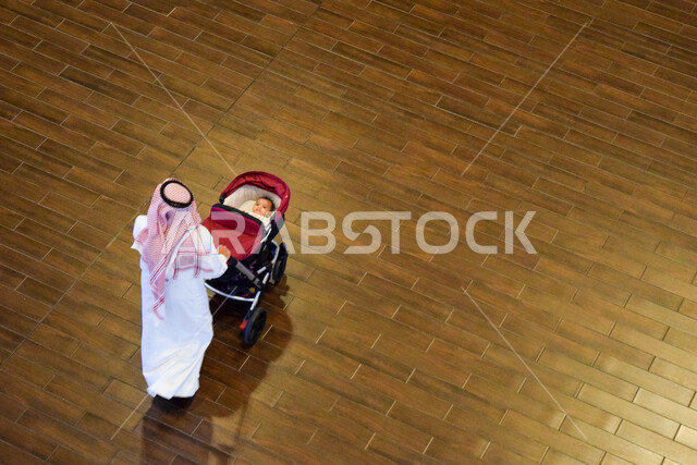 صورة من أعلى لرجل عربي خليجي يجرّ عربة طفله في نزهة عائلية بدبي بالإمارات العربية المتحدة، عربة اطفال، نزهة عائلية، السياحة في الإمارات