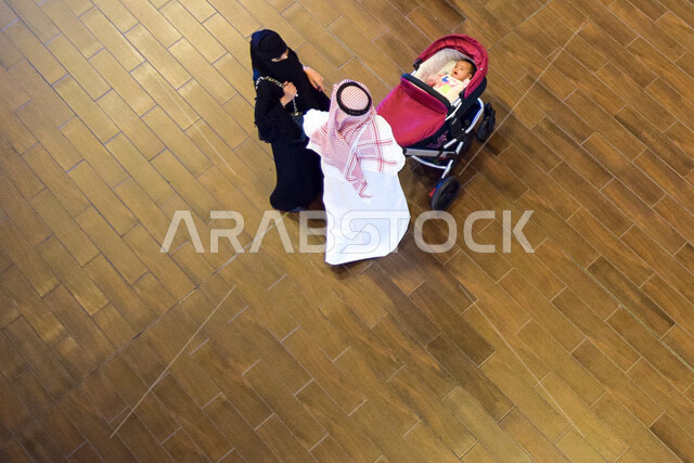A picture from above of a Gulf Arab man and his wife pulling his baby stroller on a family outing in Dubai, United Arab Emirates, baby carriage, family outing, tourism in the UAE