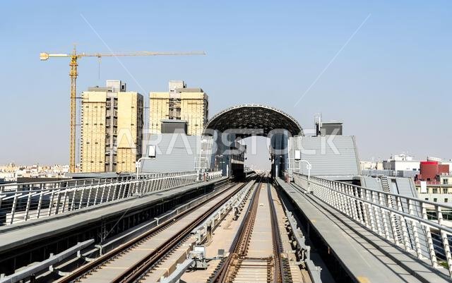 View looking down the elevated tracks of the Riyadh Metro towards the modern Granadia station with construction cranes in the background.