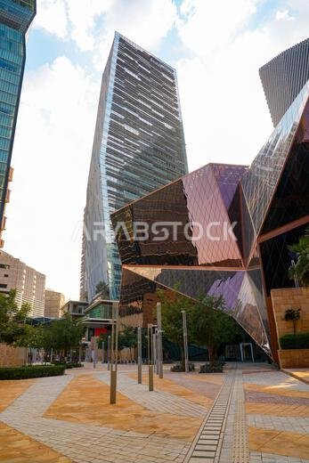 ساحة مشاة حديثة مع مبنى زجاجي هندسي نحاسي ذي تصميم مستقبلي في مركز الملك عبد الله المالي، الرياض، المملكة العربية السعودية