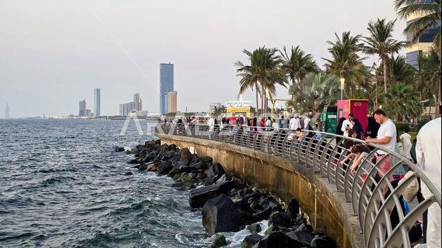 أشخاص يسترخون على رصيف الواجهة البحرية المنحني والمتنزه في كورنيش جدة الجديد، المملكة العربية السعودية