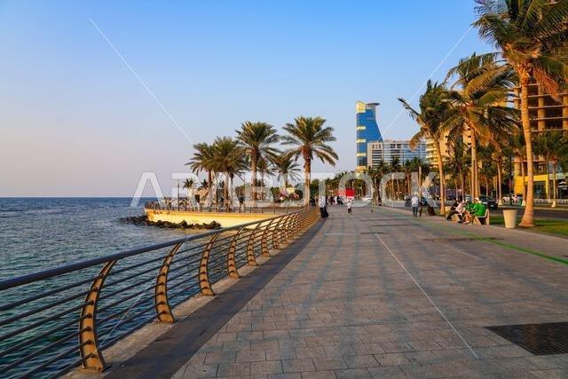 أشخاص يسترخون على رصيف الواجهة البحرية المنحني والمتنزه في كورنيش جدة الجديد، المملكة العربية السعودية