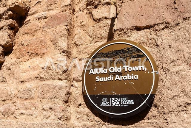 العلا، المملكة العربية السعودية - 15 فبراير 2026: لوحة تذكارية على جدار من الطوب اللبن تُعرّف مدينة العلا القديمة بأنها واحدة من أفضل القرى السياحية من قبل منظمة السياحة العالمية التابعة للأمم المتحدة في المملكة العربية السعودية.