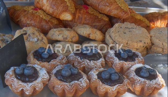 عرضٌ مغرٍ للمعجنات الطازجة المصنوعة يدويًا في سوقٍ شعبيٍّ صاخب. يضمّ كرواسون هشًّا، وكعكات رقائق الشوكولاتة الريفية، و...