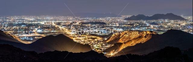 A wide panoramic night view showing the illuminated city lights of Madinah from the Jabal Uhud viewpoint in Saudi Arabia.