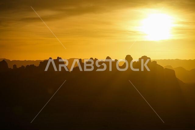 Sunrays piercing through sandstone rock silhouettes at sunrise in Hegra, AlUla
