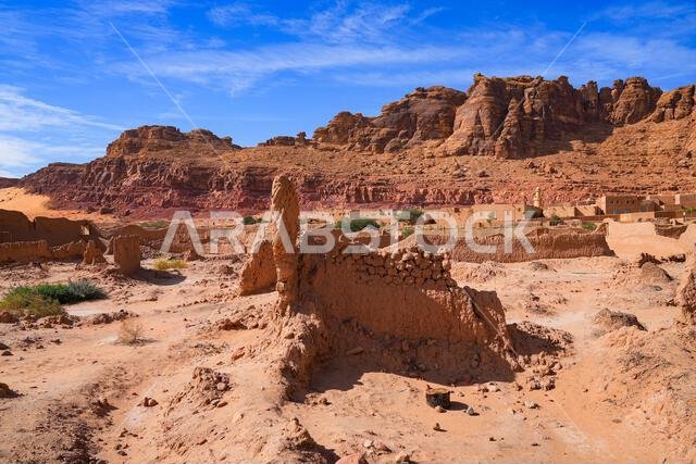 أطلال قديمة مبنية من الطوب اللبن تقع على خلفية جبال من الحجر الرملي الأحمر في واحة العلا التاريخية التراثية، المملكة العربية السعودية